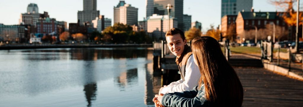 Male and female Providence College students look over the river with the city skyline behind